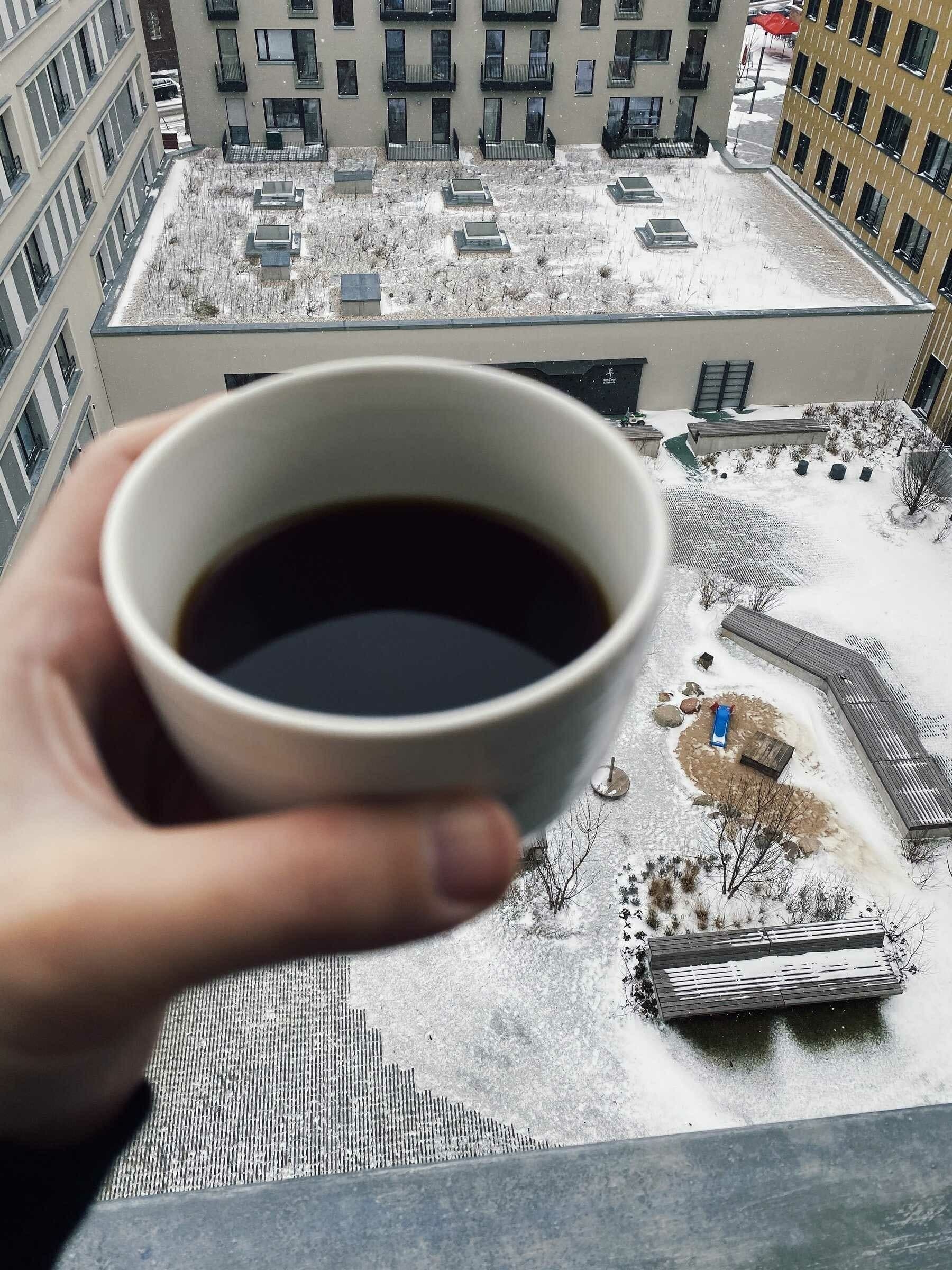 a hand holding a cup of coffee in the balcony with view of backyard covered in snow; with the backyard in focus