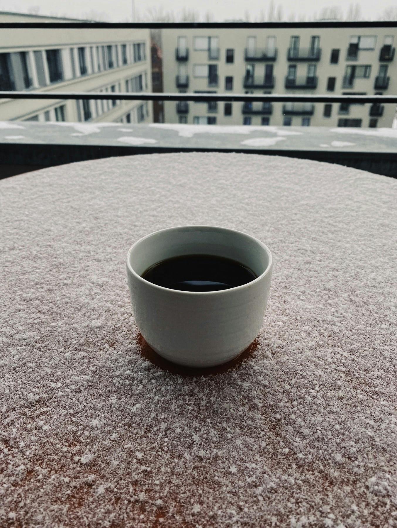 cup of coffee, over a table in a balcony covered in snow