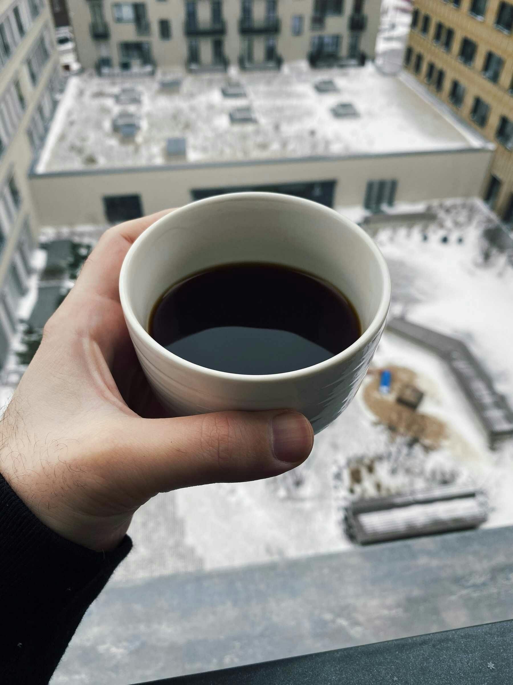 a hand holding a cup of coffee in the balcony with view of backyard covered in snow; with the cup is in focus