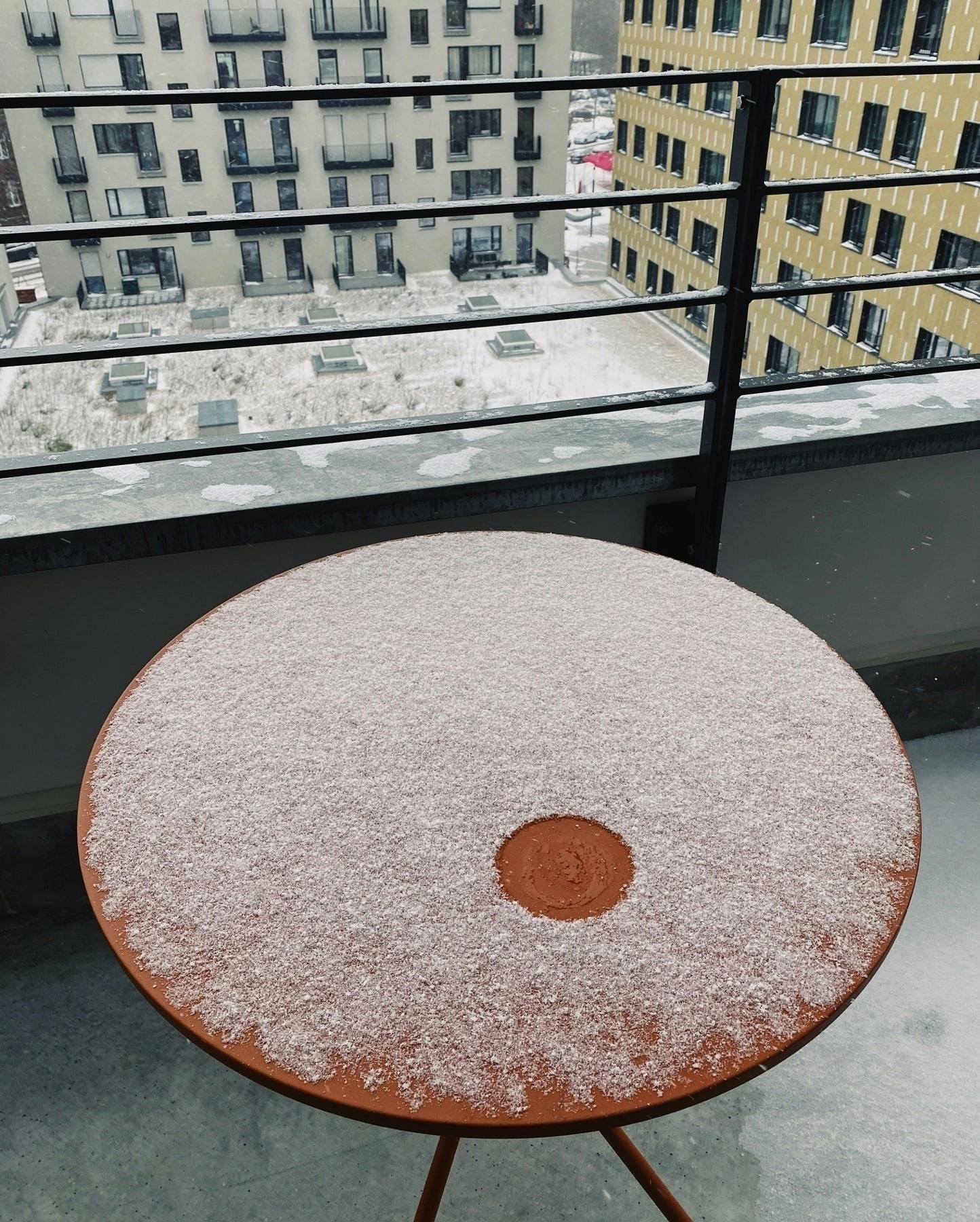 a table in a balcony covered in snow, some snow is melted making an empty circular shape